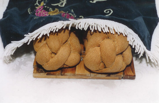 Two challah loaves covered with a decorative challah cloth on a Shabbat table
