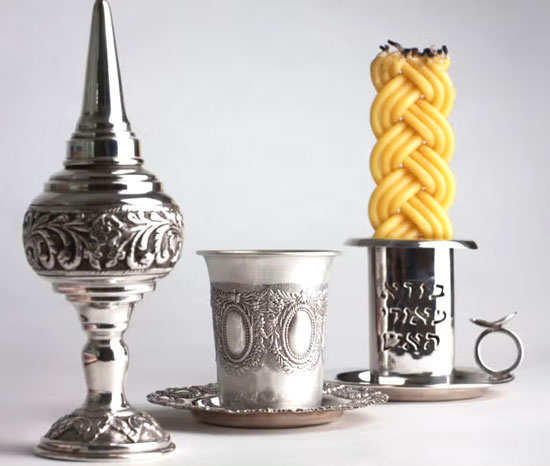 Braided Havdalah candle lit beside a cup of wine and a spice box